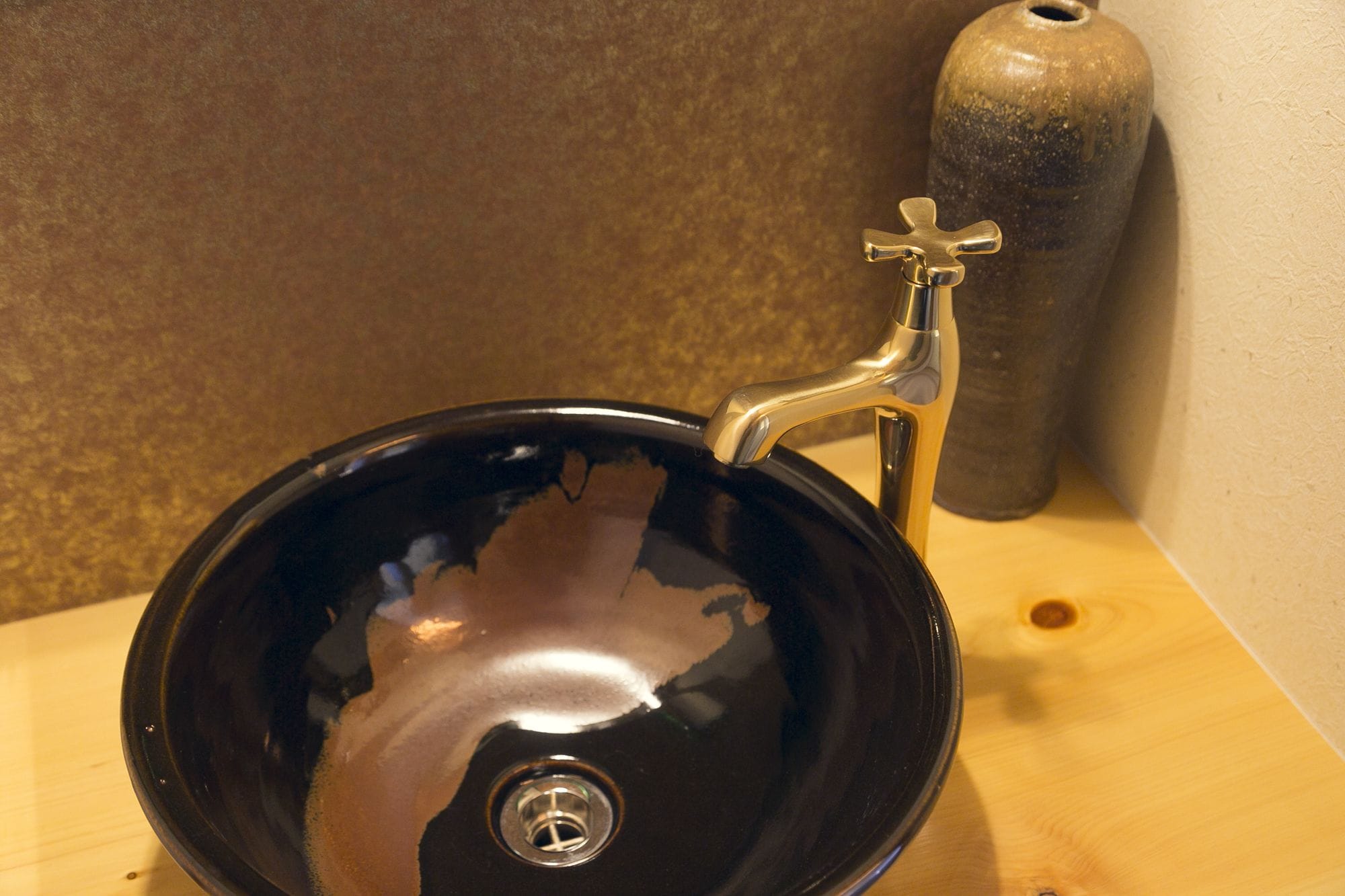 A black, glossy, round sink with a single faucet on a wooden surface.