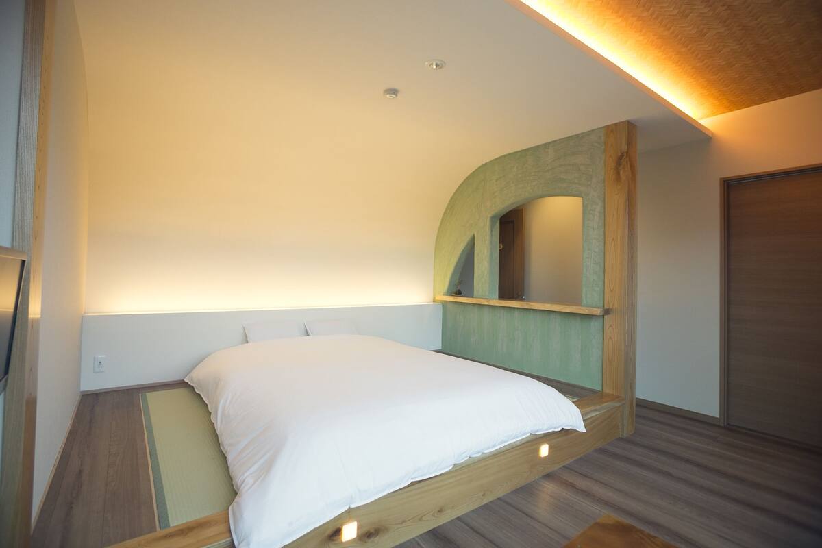 Una cama individual con estructura de madera y colchón blanco en una habitación con techo inclinado y suelo de madera.