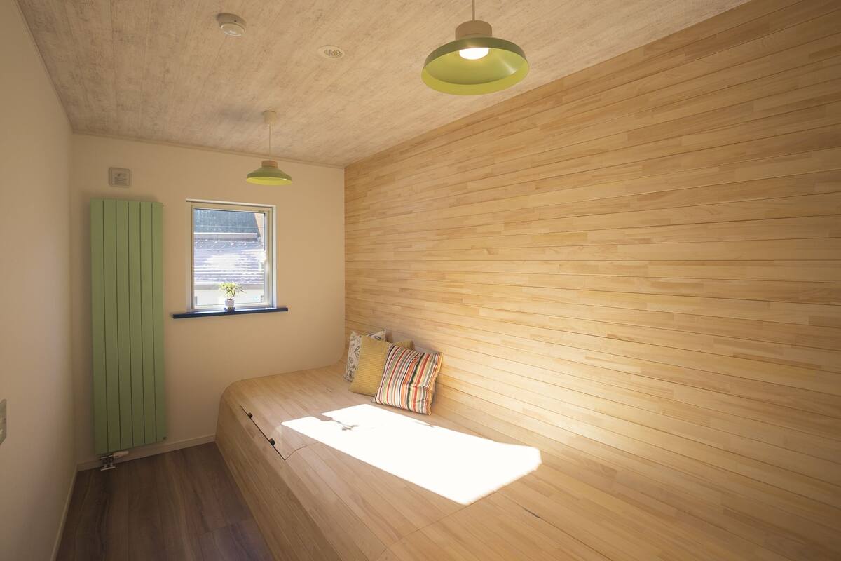 Una habitación con pared de listones de madera, ventana con vistas, cama con almohadas y una lámpara colgante verde.