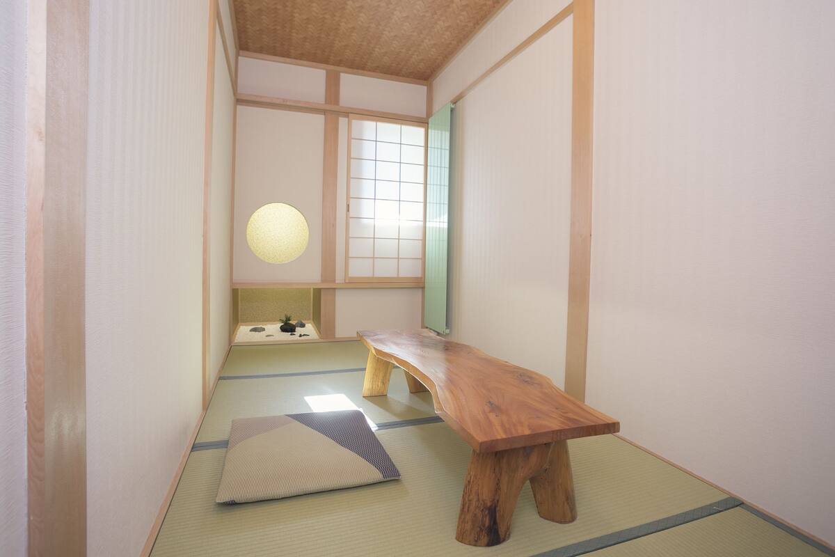 Una habitación japonesa tradicional con suelo de tatami, un banco de madera, un celosía japonesa y una lámpara colgante.