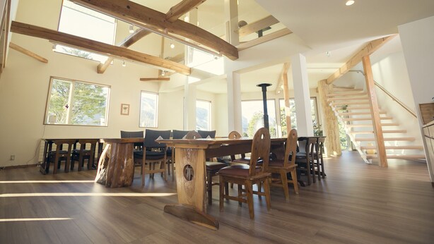 A spacious dining area with wooden beams, large windows, and a staircase. - Ryokan Mokuzin (Hakuba)