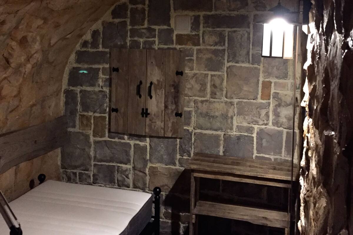 Habitación de paredes de piedra con una cama de madera, una mesita y un armario.
