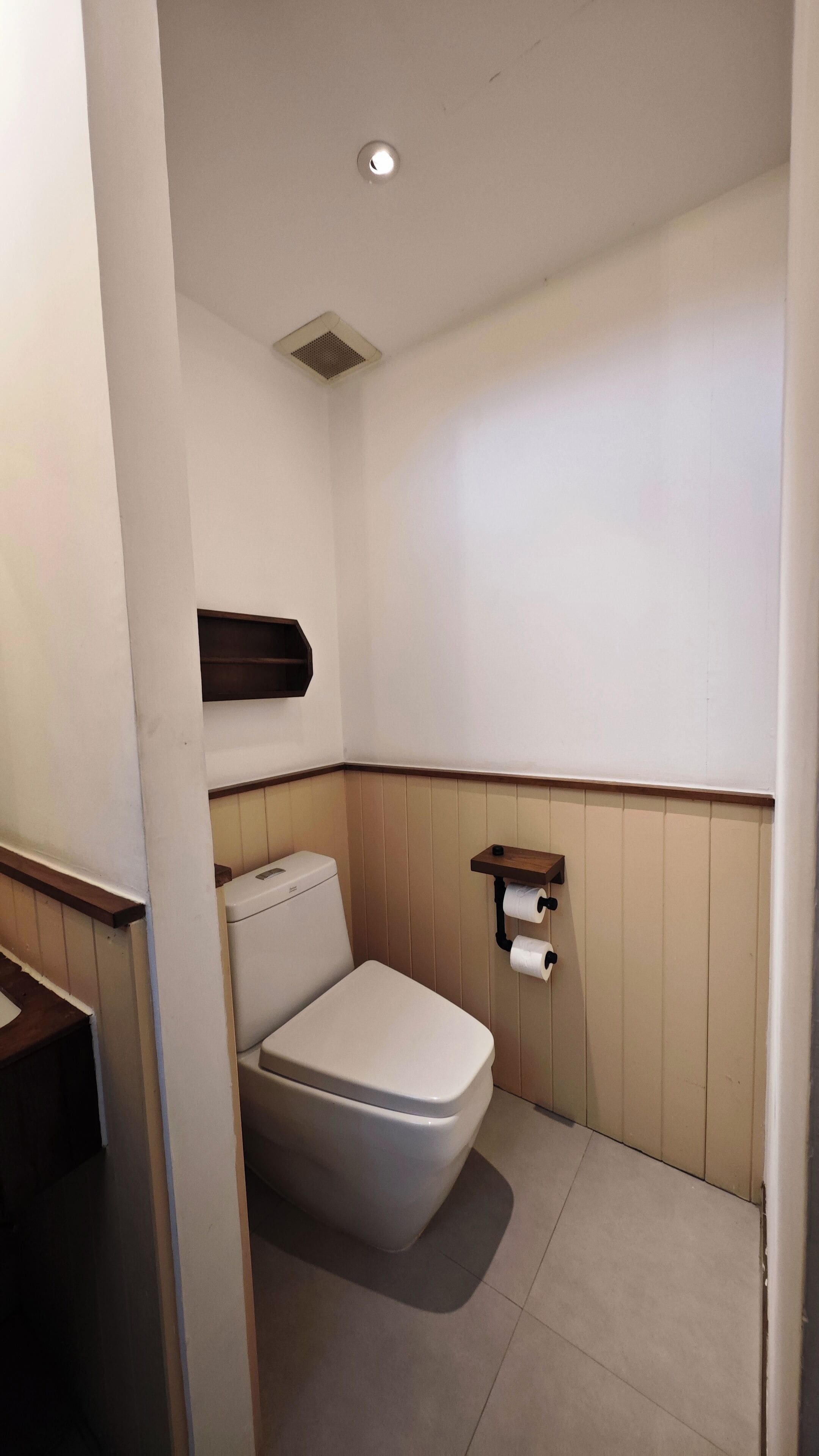 A small, compact bathroom with a toilet, a wall-mounted shelf, and a toilet paper holder.