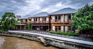 Un hotel frente al río con fachada de madera, varios balcones y un paseo a orillas del río.