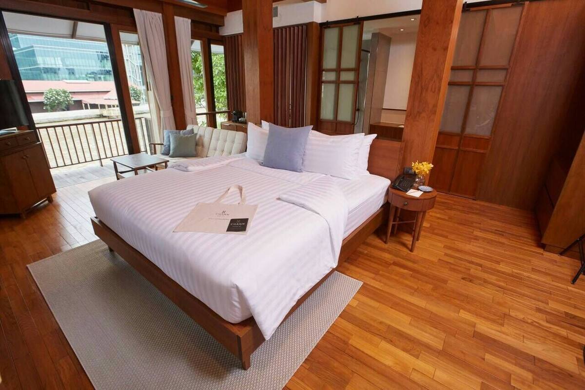 Quarto espaçoso com uma cama grande, piso de madeira, varanda com cadeira e vista para o exterior.