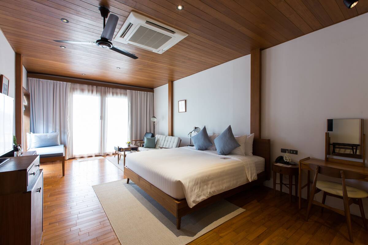 Quarto moderno com uma cama grande, piso de madeira, ventilador de teto e uma escrivaninha com cadeira.