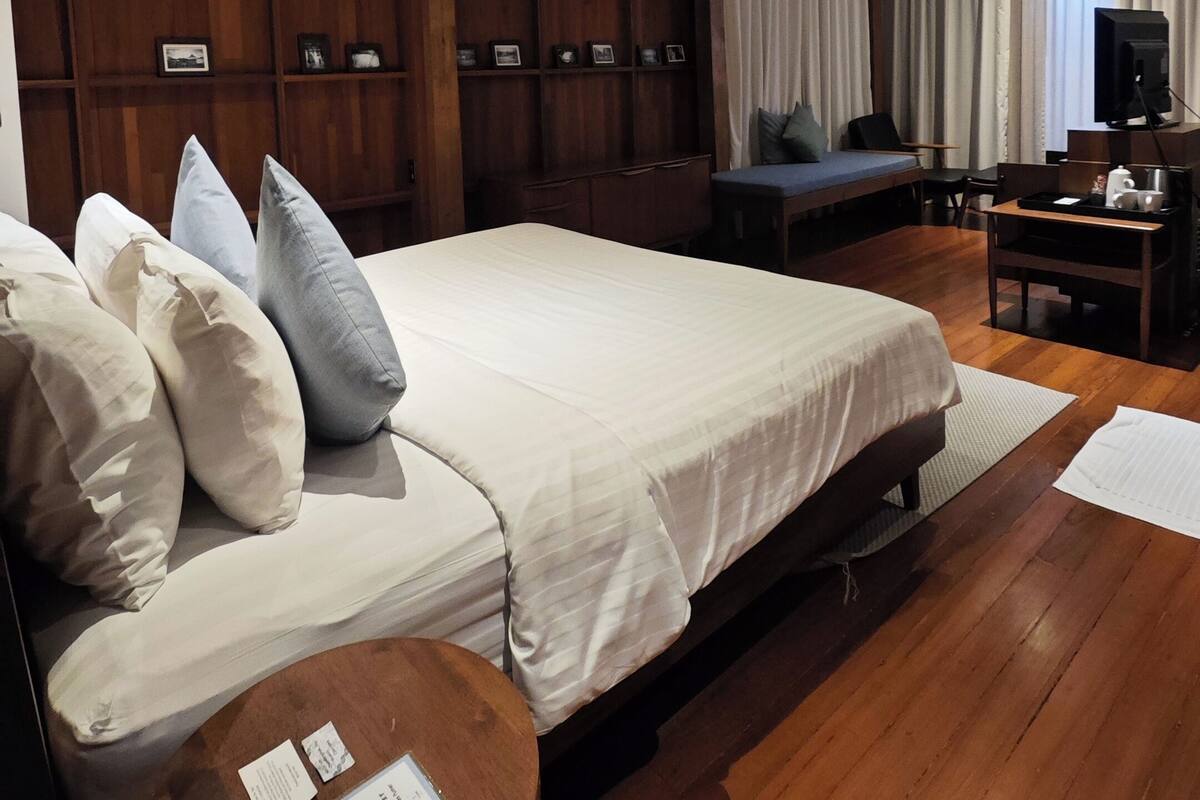 Quarto de hotel moderno com uma cama grande, painéis de madeira, uma mesa de escritório com televisão e um ventilador de teto.