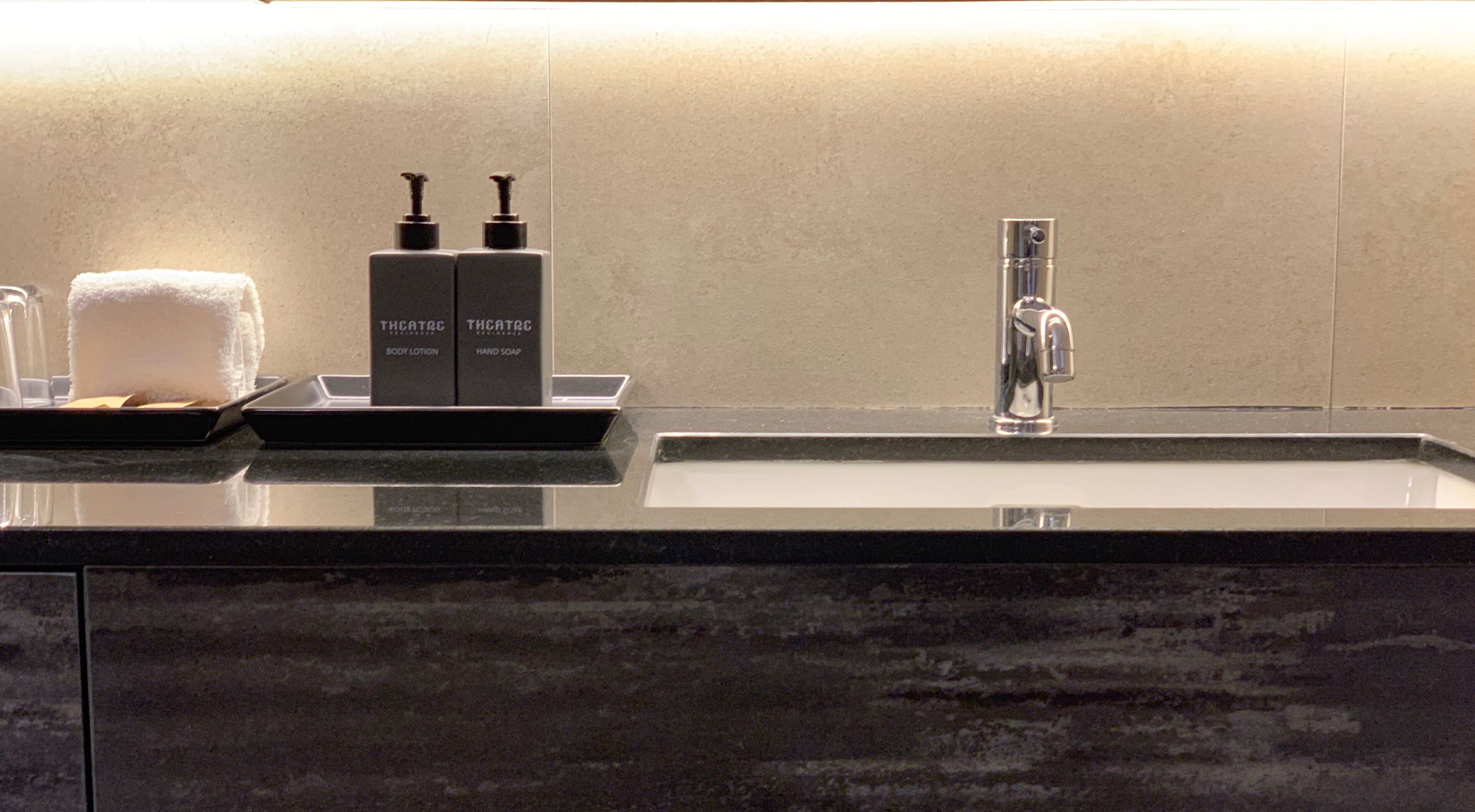 Une salle de bain avec un comptoir en marbre, un lavabo, un miroir et deux flacons de lotion pour le corps et de savon pour les mains de la marque THCATRC.