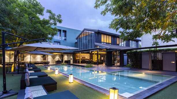 A modern outdoor pool area with lounge chairs and umbrellas, surrounded by buildings and trees. - Theatre Residence (Bangkok)