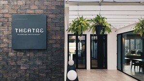 A modern restaurant entrance with a brick wall, a signboard, and indoor plants. - Theatre Residence (Bangkok)