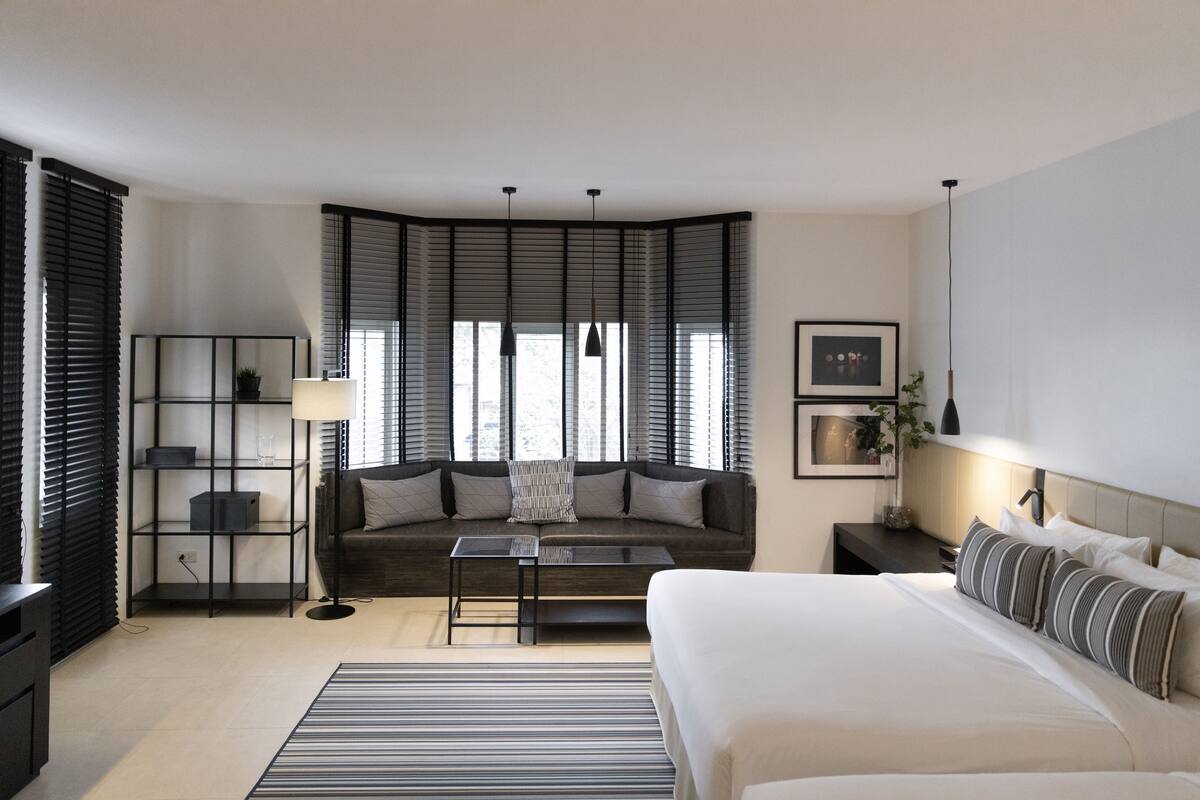 Moderni hotellihuone, jossa on suuri sänky, sohva, pieni pöytä ja kirjahylly.