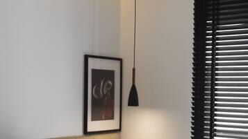 A bedroom with a bed, a framed picture on the wall, a bedside table, and a window with blinds.
