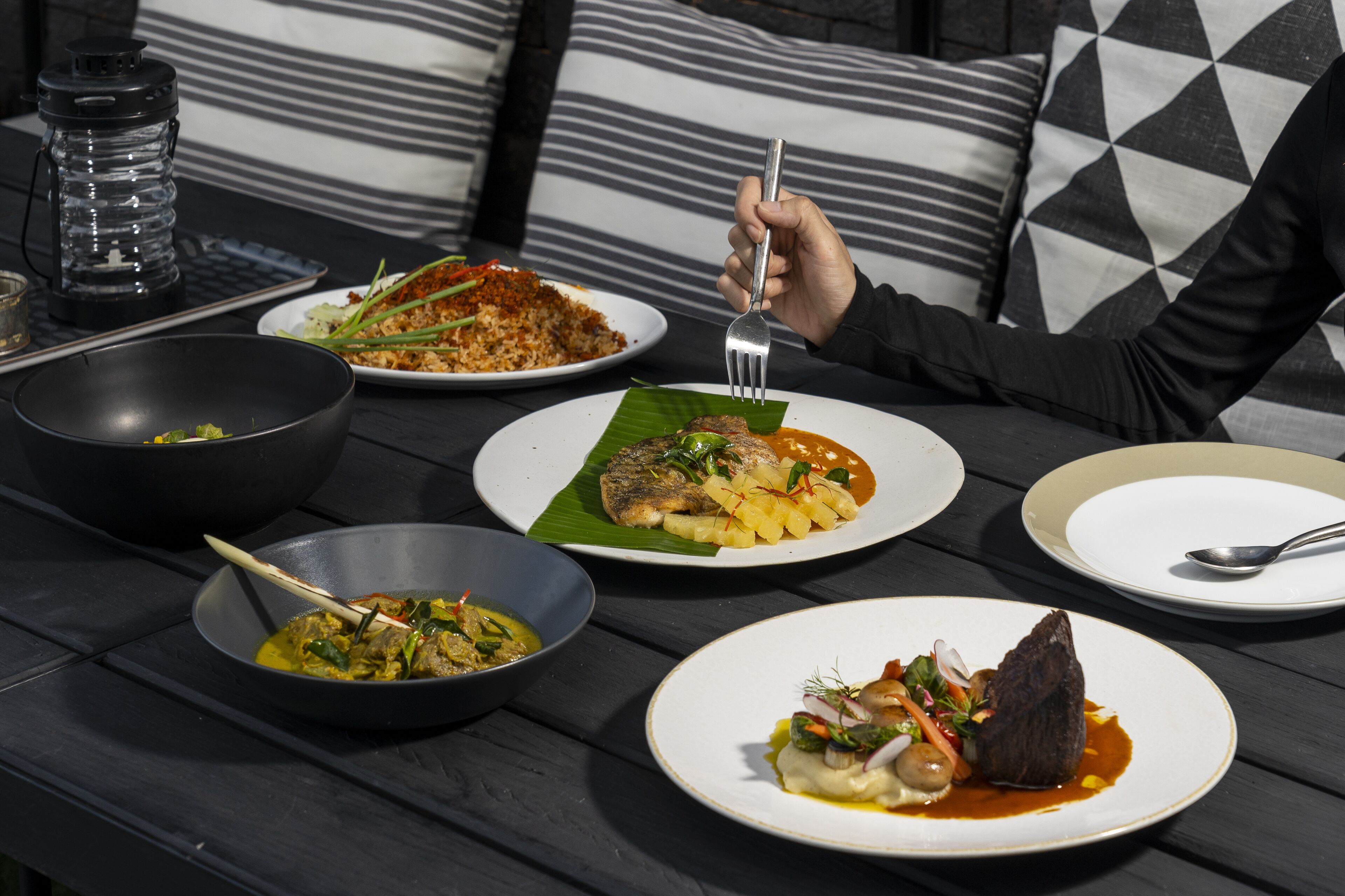 A dining table with various dishes, a person holding a fork, and a water bottle.
