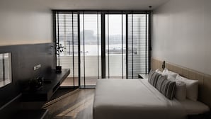 A modern hotel room with a bed, a desk, and a large window with blinds. - Theatre Residence (Bangkok)