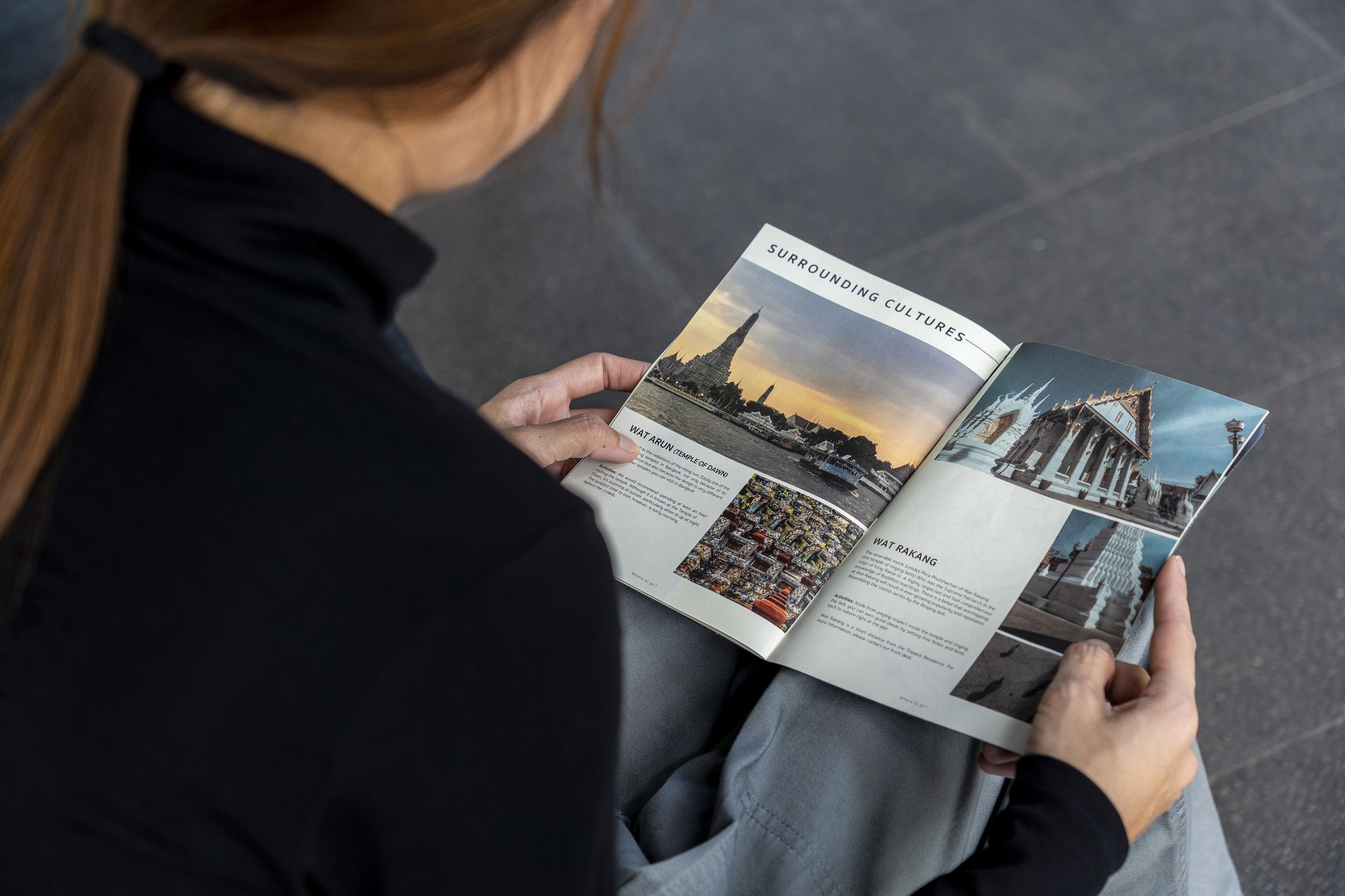 A person holding a magazine with pages featuring images of Wat Arun and Wat Makang temples.