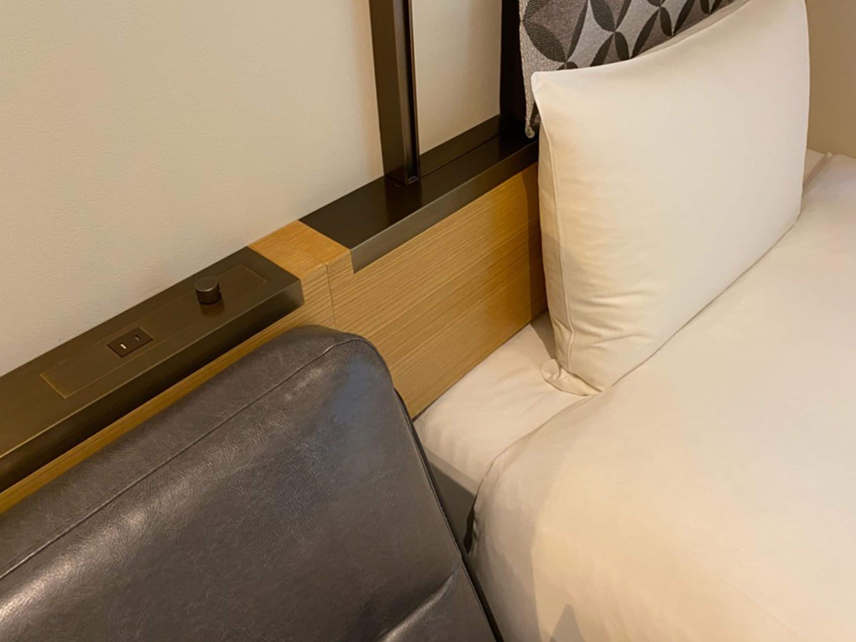 Una habitación de hotel con cabecera de madera, una mesita de noche con lámpara y una cama individual con ropa de cama blanca.