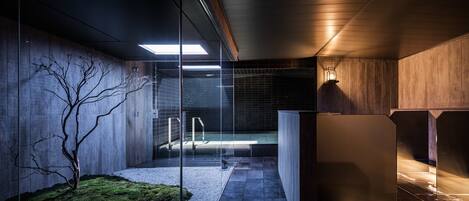 A modern interior with a glass partition, a minimalist design, and a small outdoor area with a tree and gravel path.