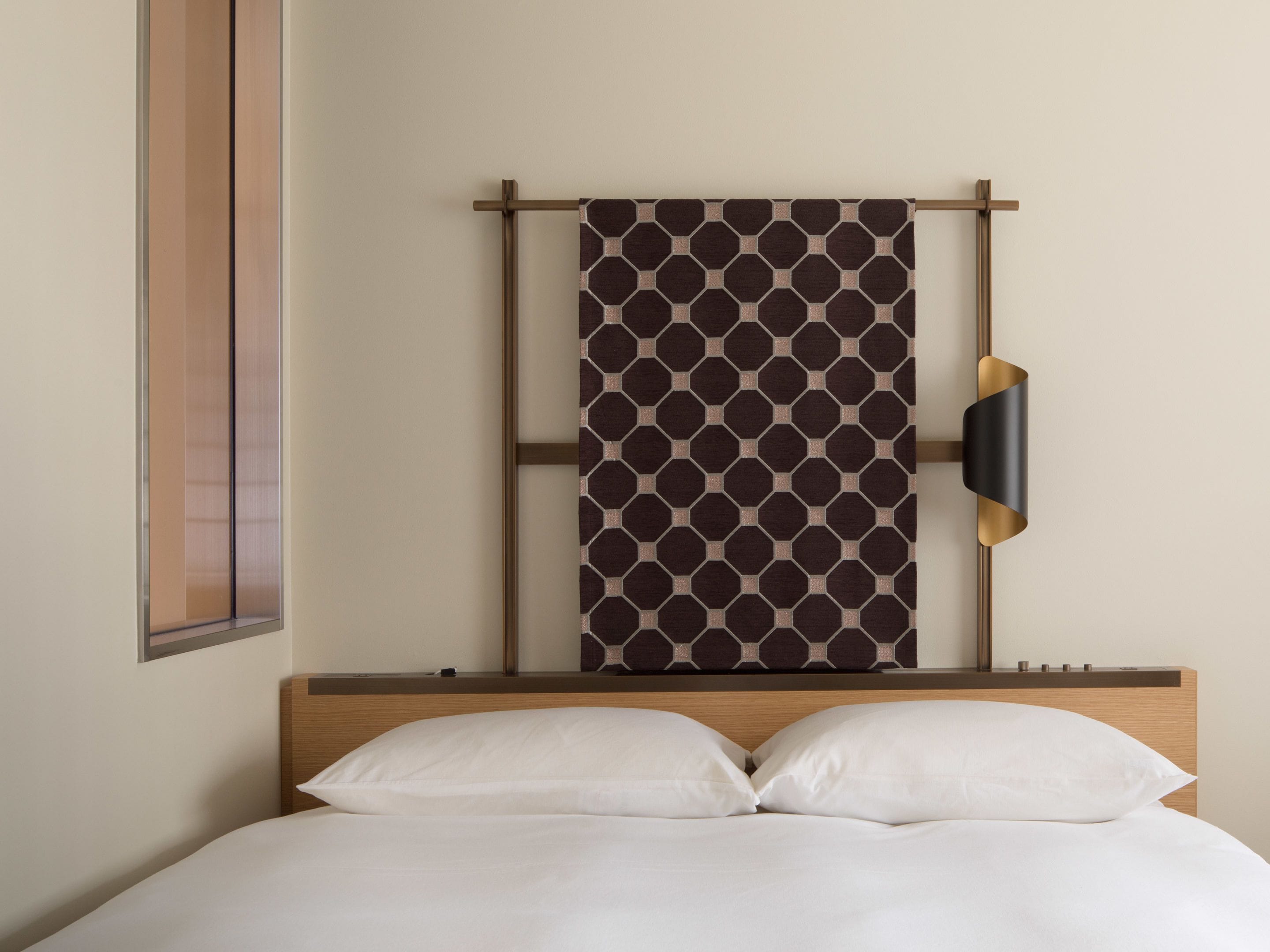 Une chambre à coucher avec un lit, une tête de lit, un luminaire fixé au mur et un rideau à motifs.