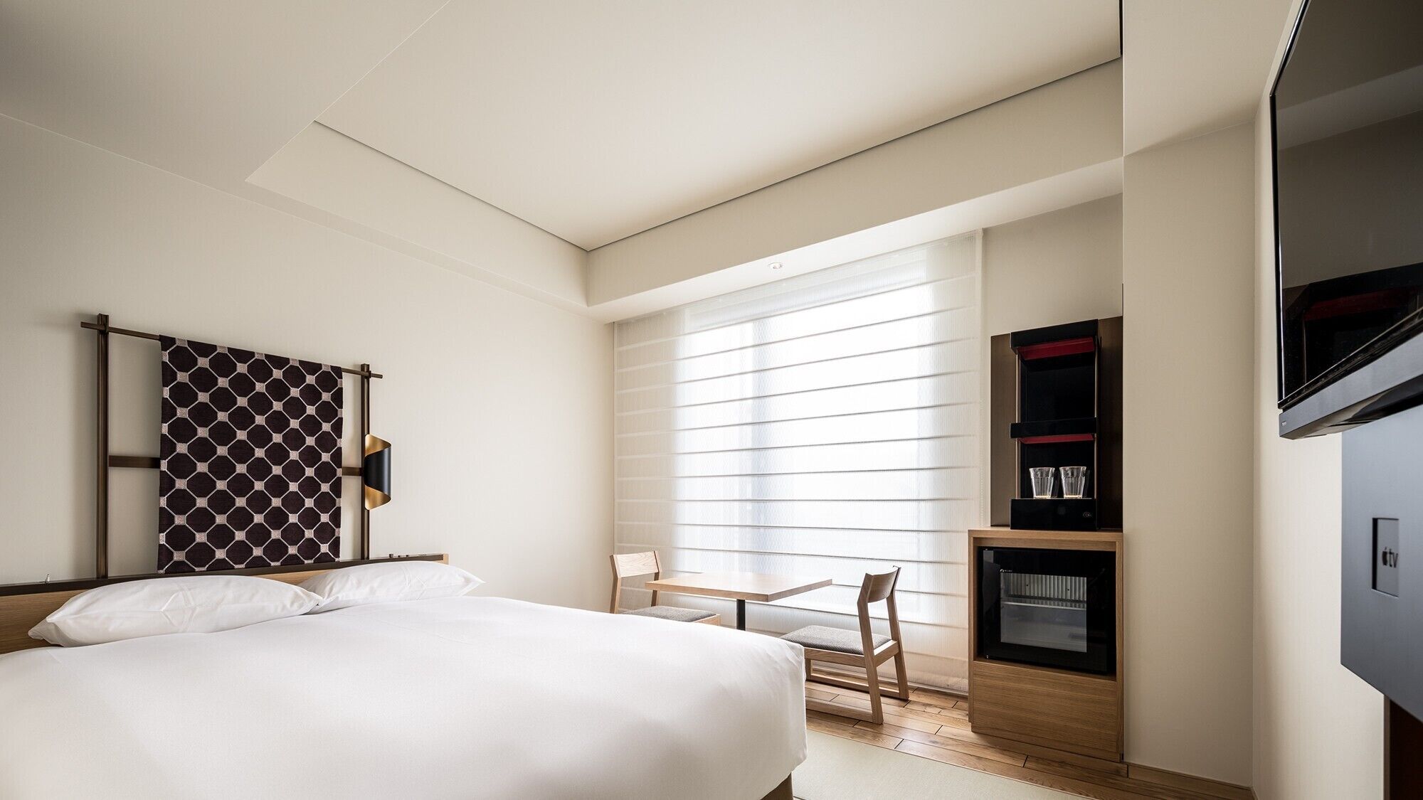 Una habitación de hotel con cama, escritorio, televisor y ventana con persianas.