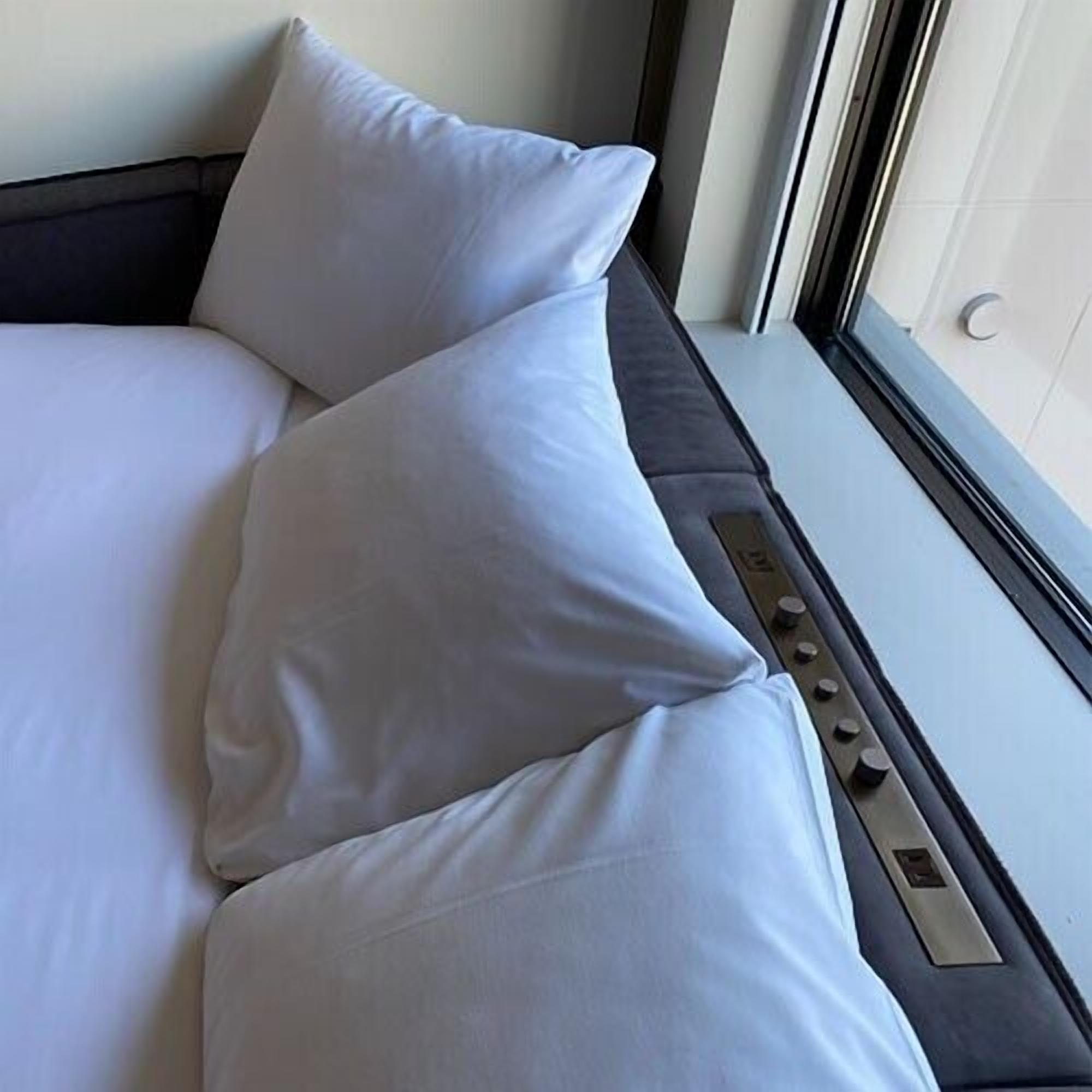 A bed with white bedding and pillows, a window with blinds, and a control panel on the side.