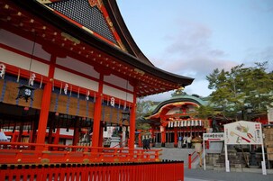 A traditional Japanese temple with red and black architecture, a curved roof, and a stone lantern in the foreground.