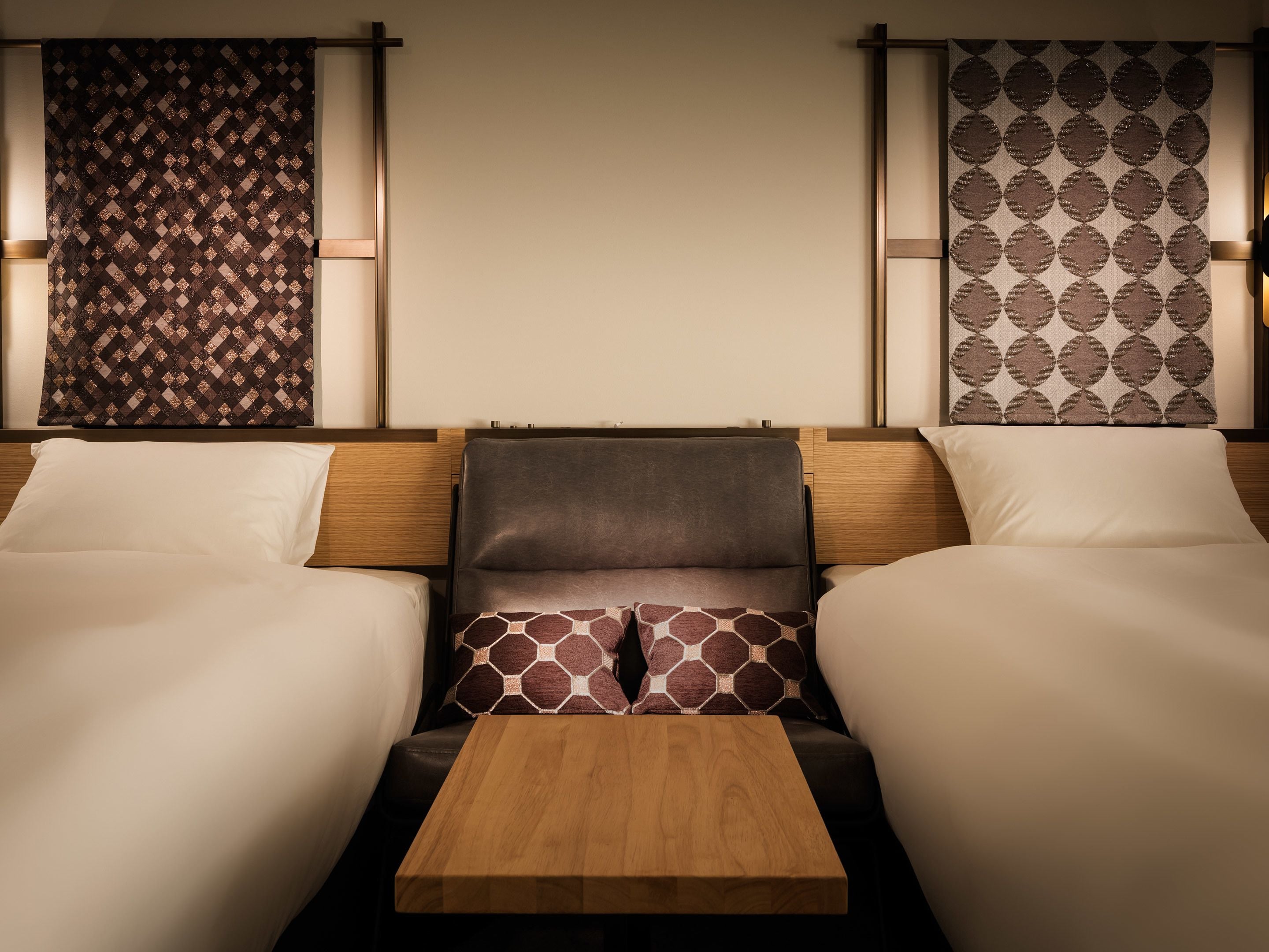 A hotel room with two beds, a wooden table, and patterned headboards.