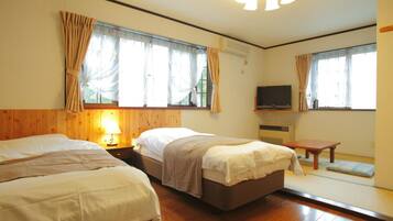 A hotel room with two beds, a TV, a small table, and a window with curtains.
