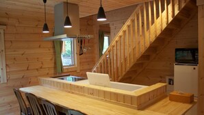 Interior de una cabaña de madera con cocina, comedor y escalera.