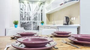 Una cucina moderna con mobili bianchi, un lavello e un bollitore. Si vede un tavolo da pranzo con piatti viola e posate.