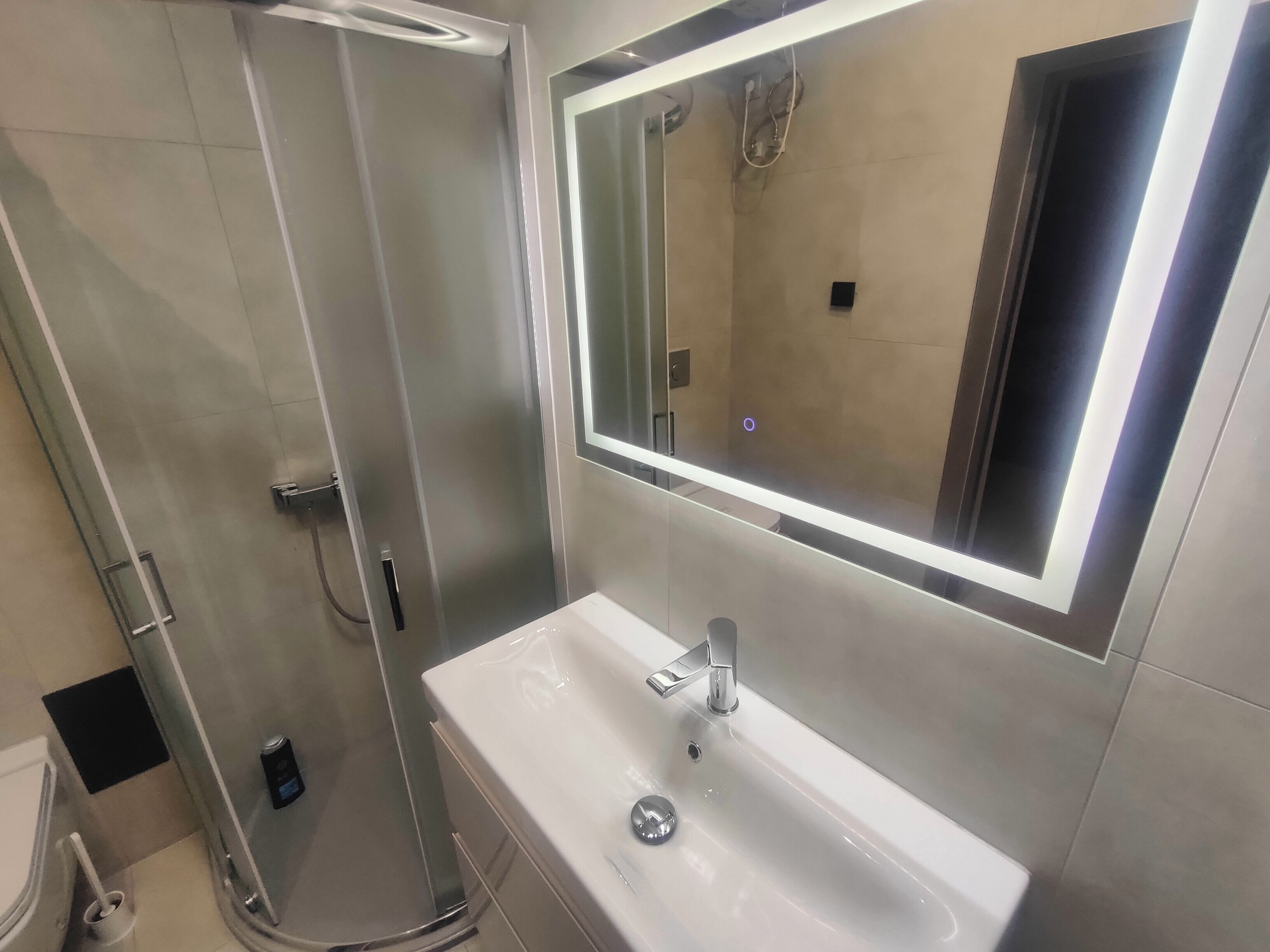 A modern bathroom with a glass-enclosed shower, a white sink with a mirror above it, and a visible shower control panel.