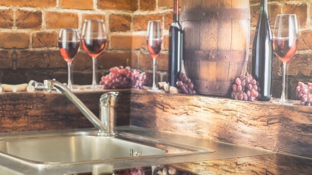 Una cucina con lavello in acciaio inossidabile, un piano di lavoro in legno e un muro di mattoni sullo sfondo.