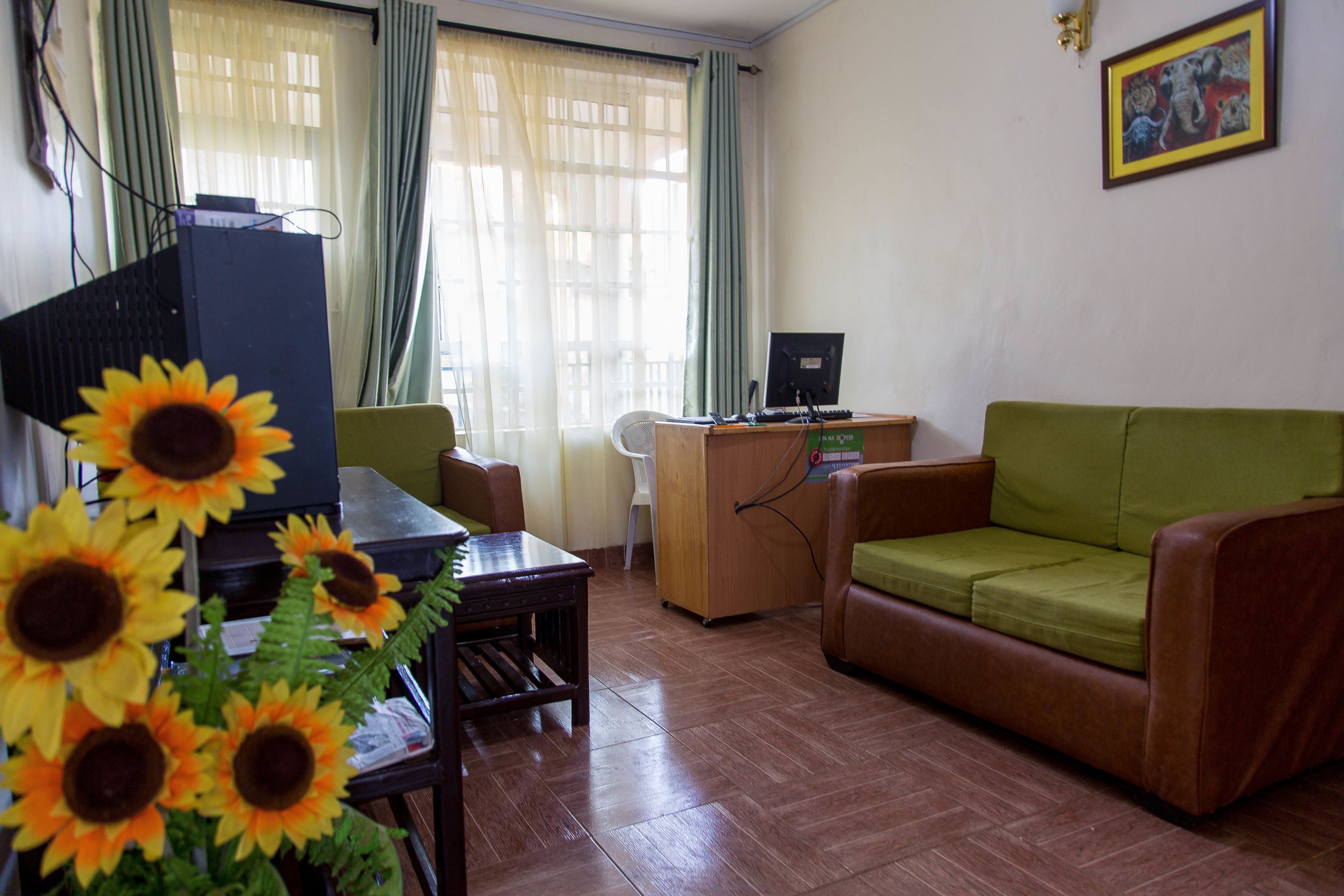 Una sala de estar con un escritorio de madera, un sofá verde y un televisor. Hay girasoles sobre la mesa.