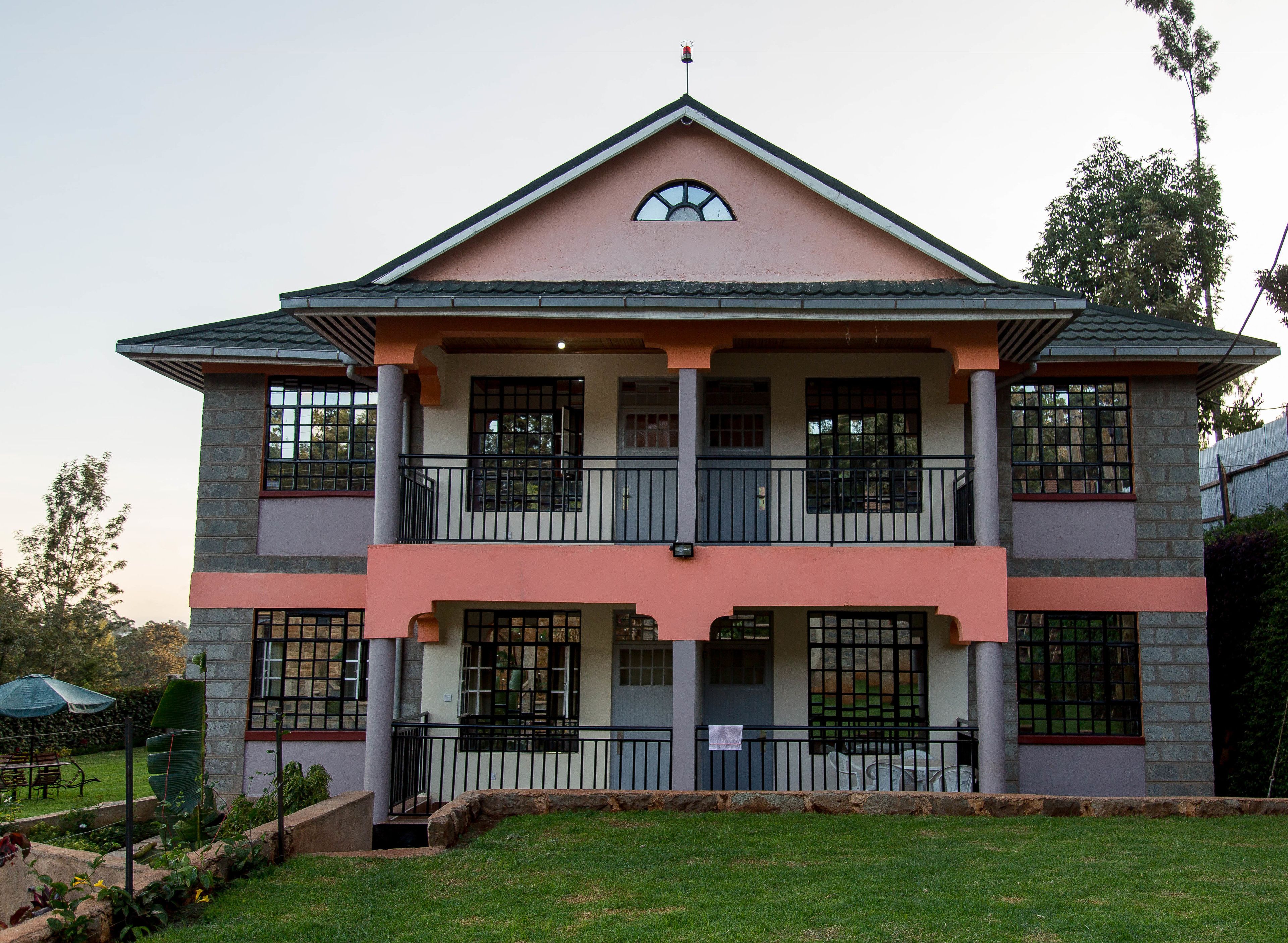 A two-story building with a symmetrical facade, featuring a central balcony with railings, multiple windows, and a small overhang above the entrance.
