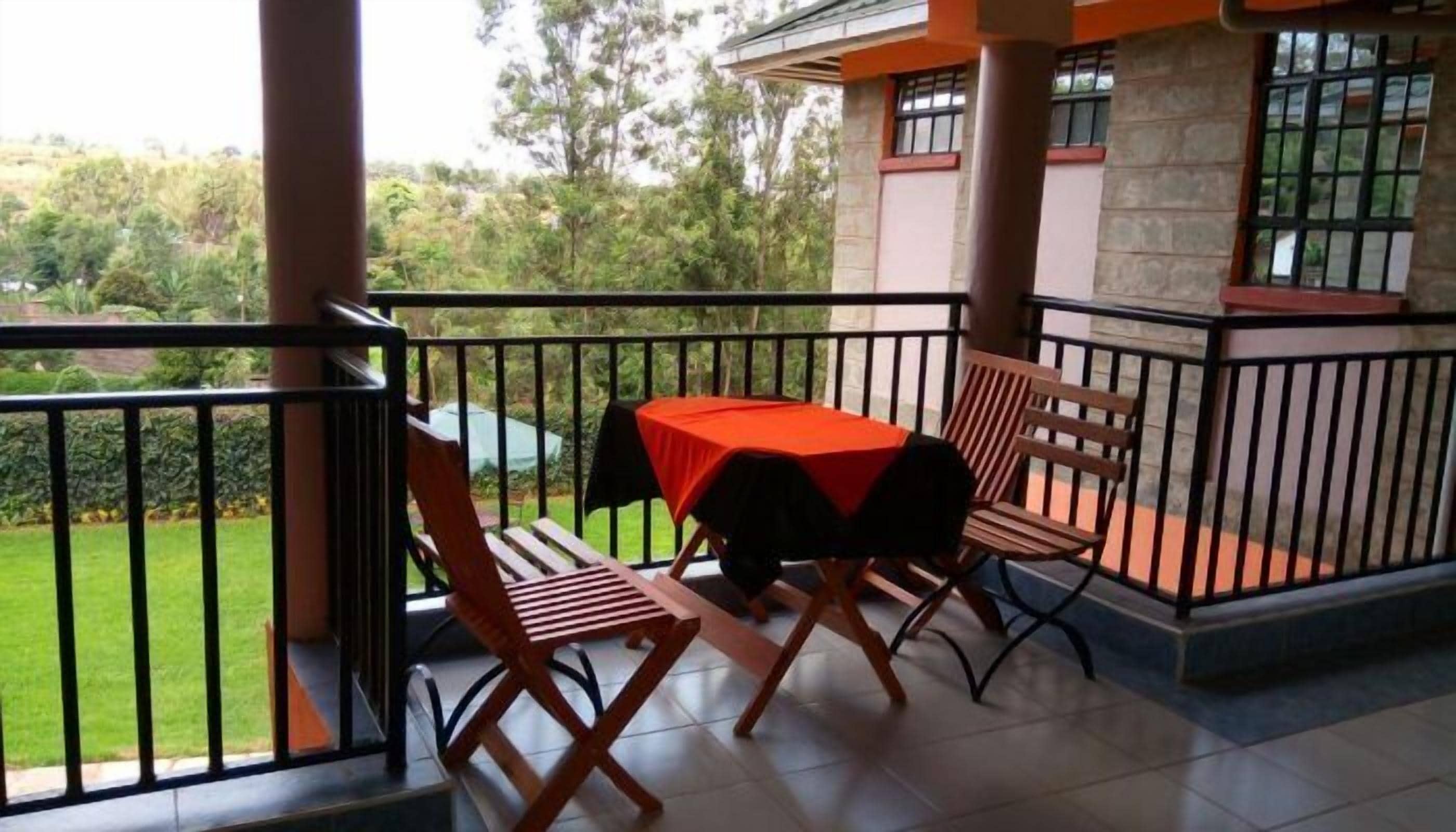 A balcony with a table and two chairs, a view of greenery, and a stone building in the background.