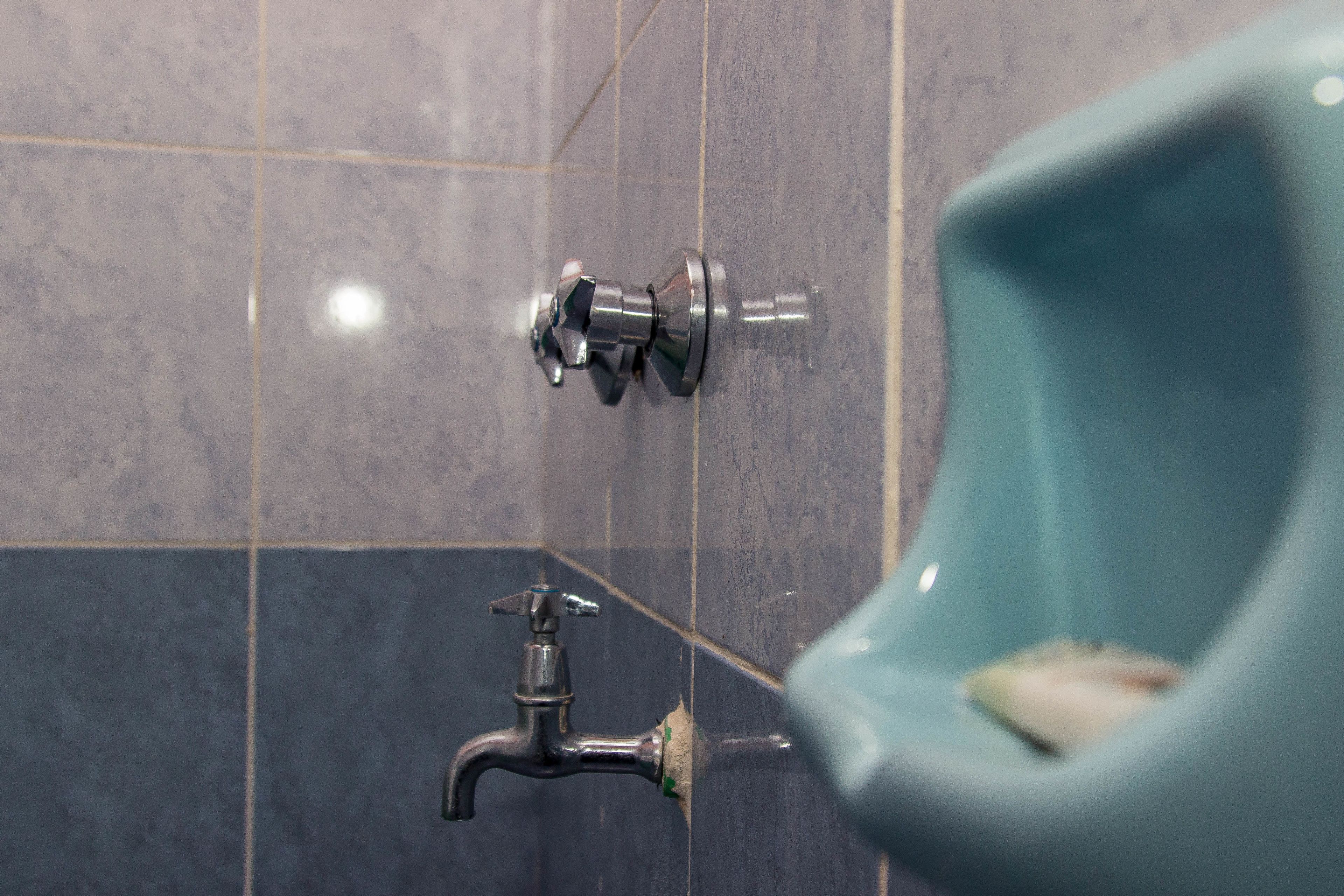 A bathroom with a urinal, a faucet, and tiled walls.