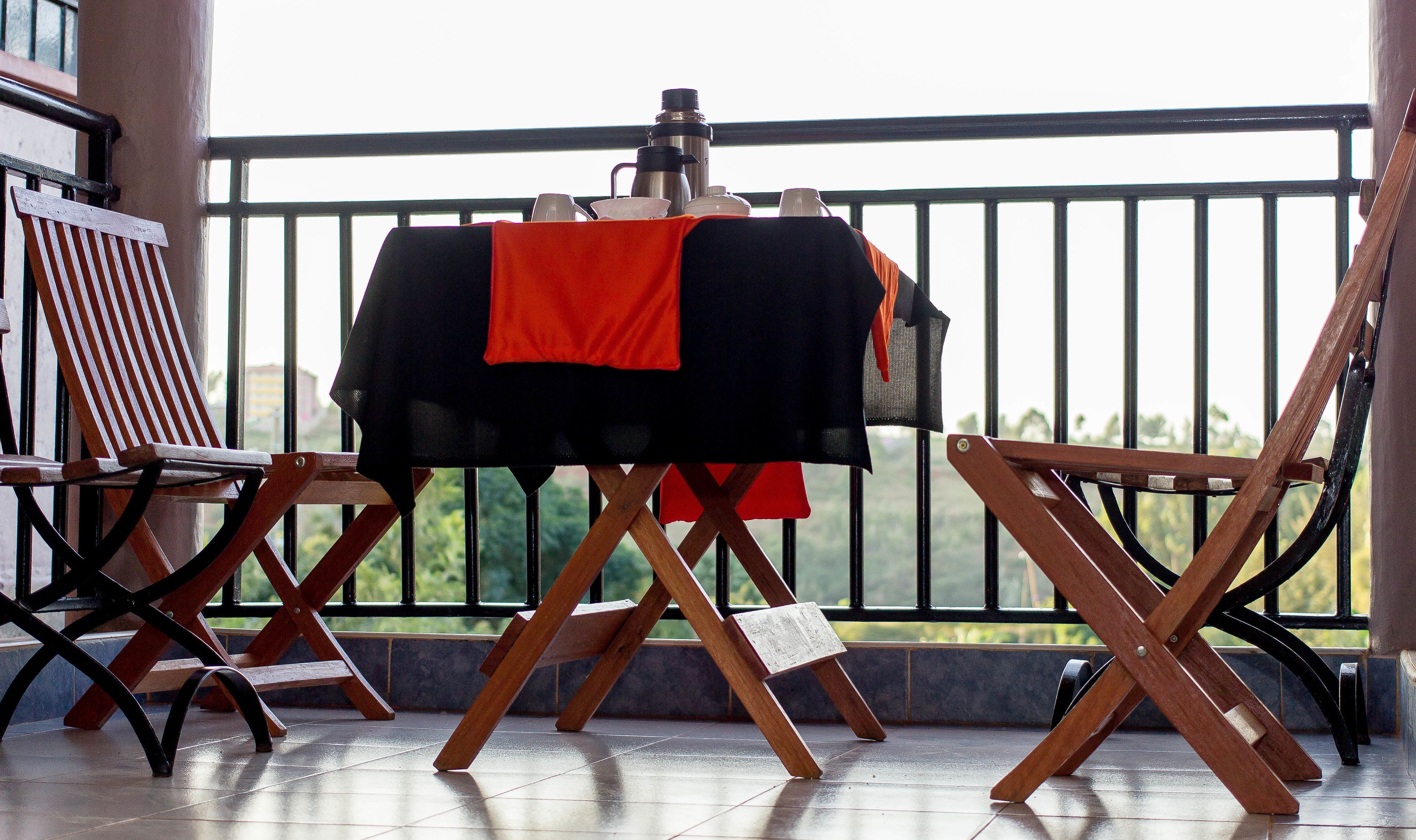 A balcony with a table set for a meal, a chair, and a view of greenery.