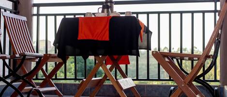 A balcony with a table set for a meal, a chair, and a view of greenery.