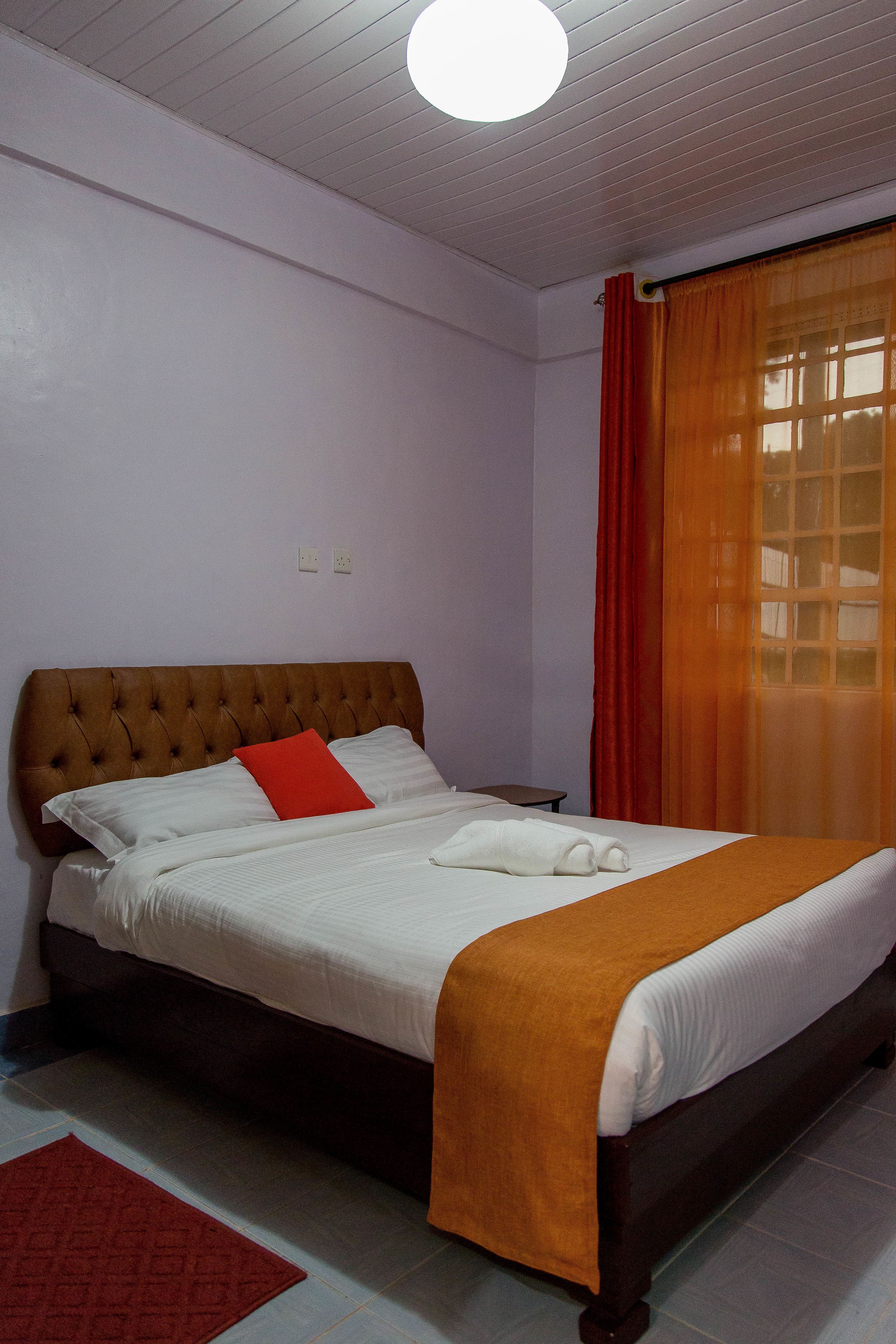 A neatly made bed with a brown headboard, white bedding, and a red accent pillow.
