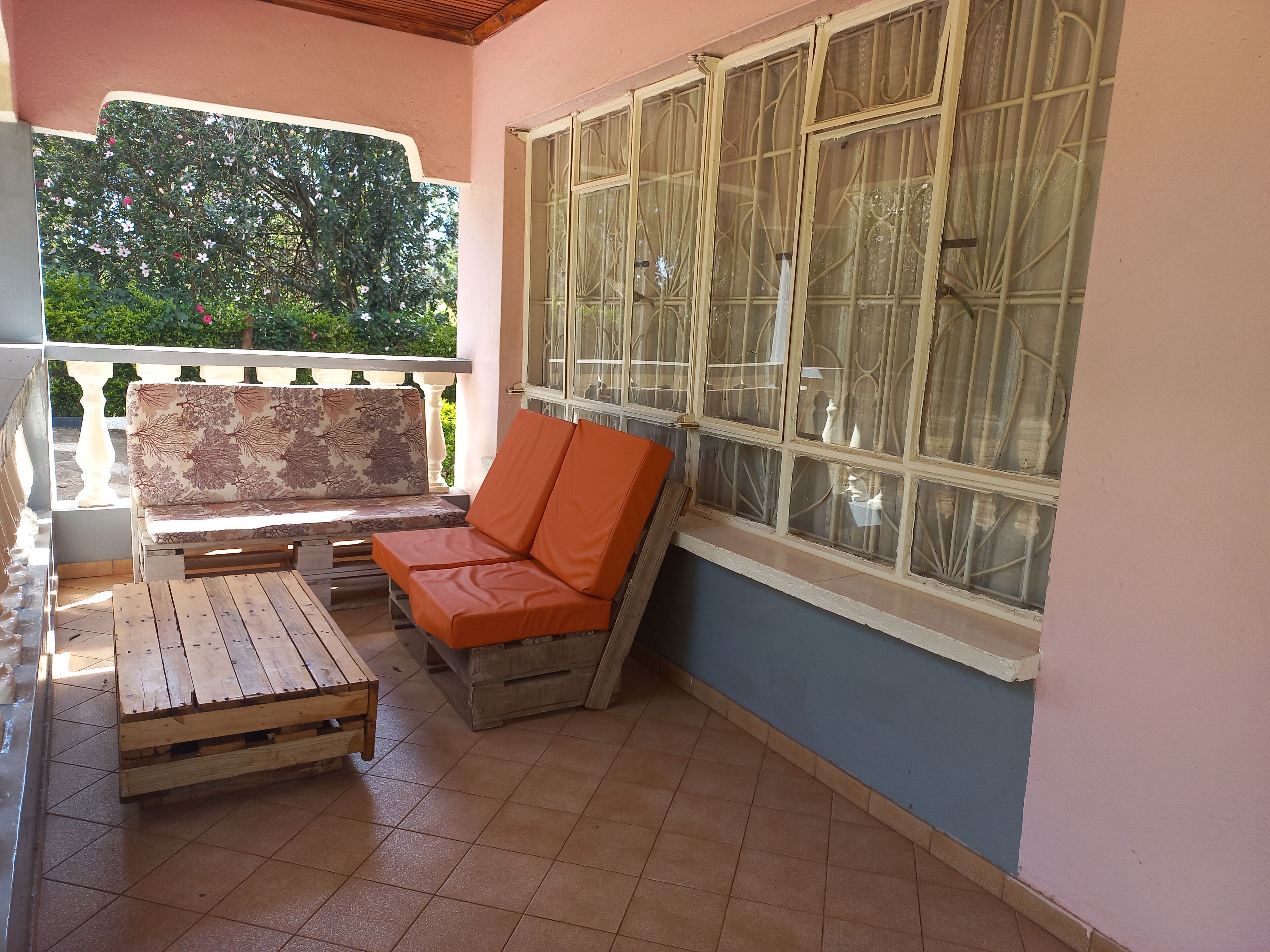 Un patio cubierto con un banco de madera, una silla acolchada y un ventanal con vidrieras decorativas.