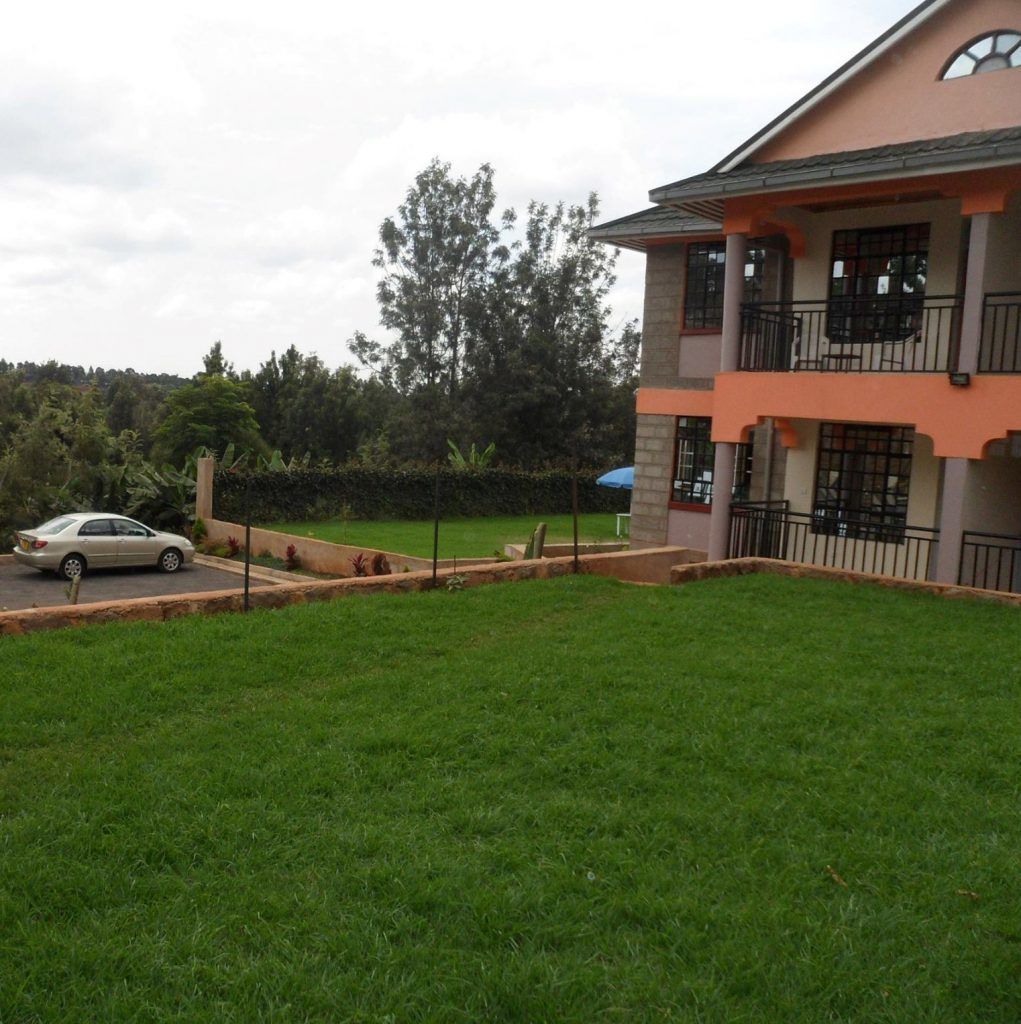 A two-story building with a balcony, a car parked in front, and a well-maintained lawn.
