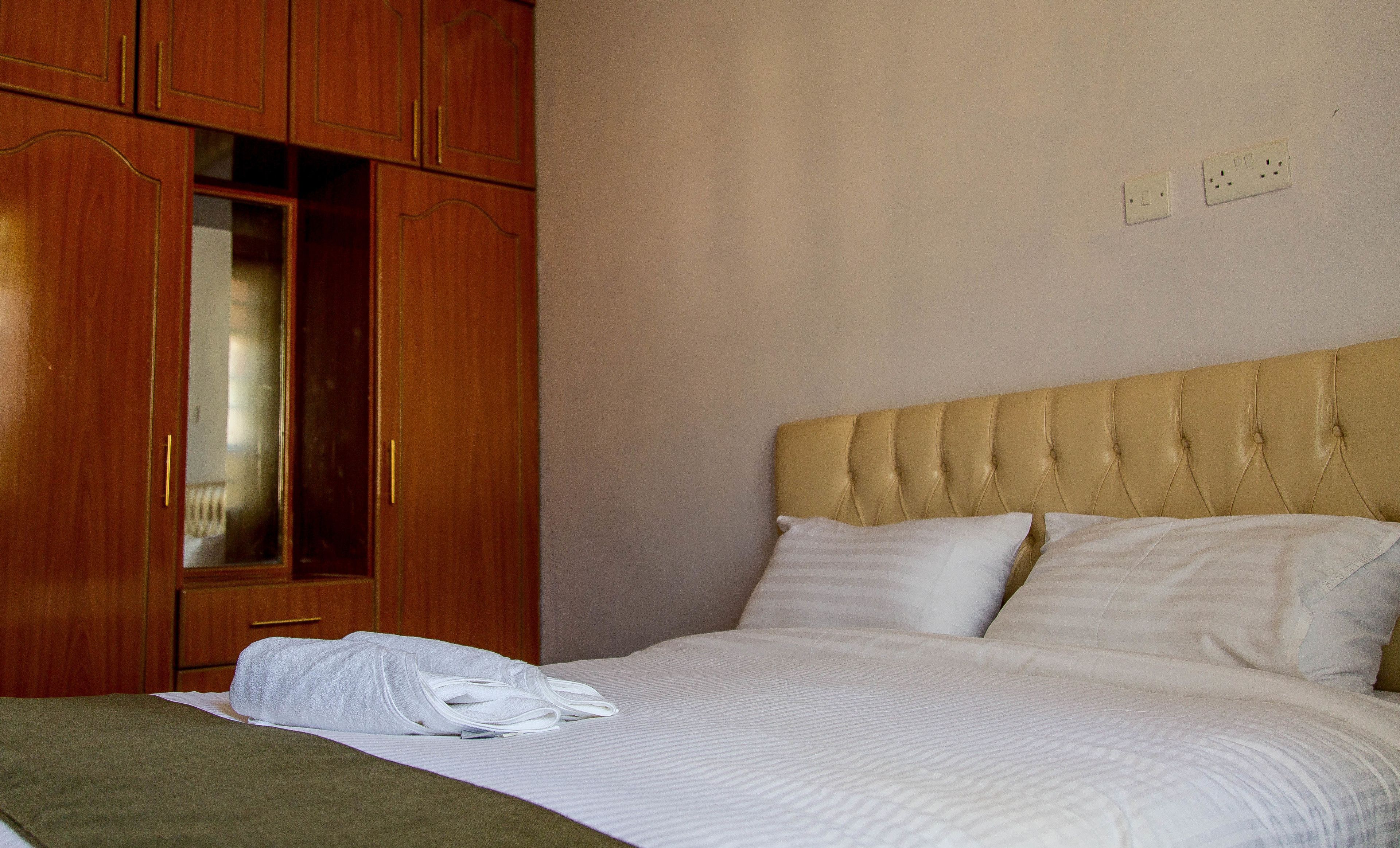A hotel room with a bed, a wooden wardrobe, and a wall socket.