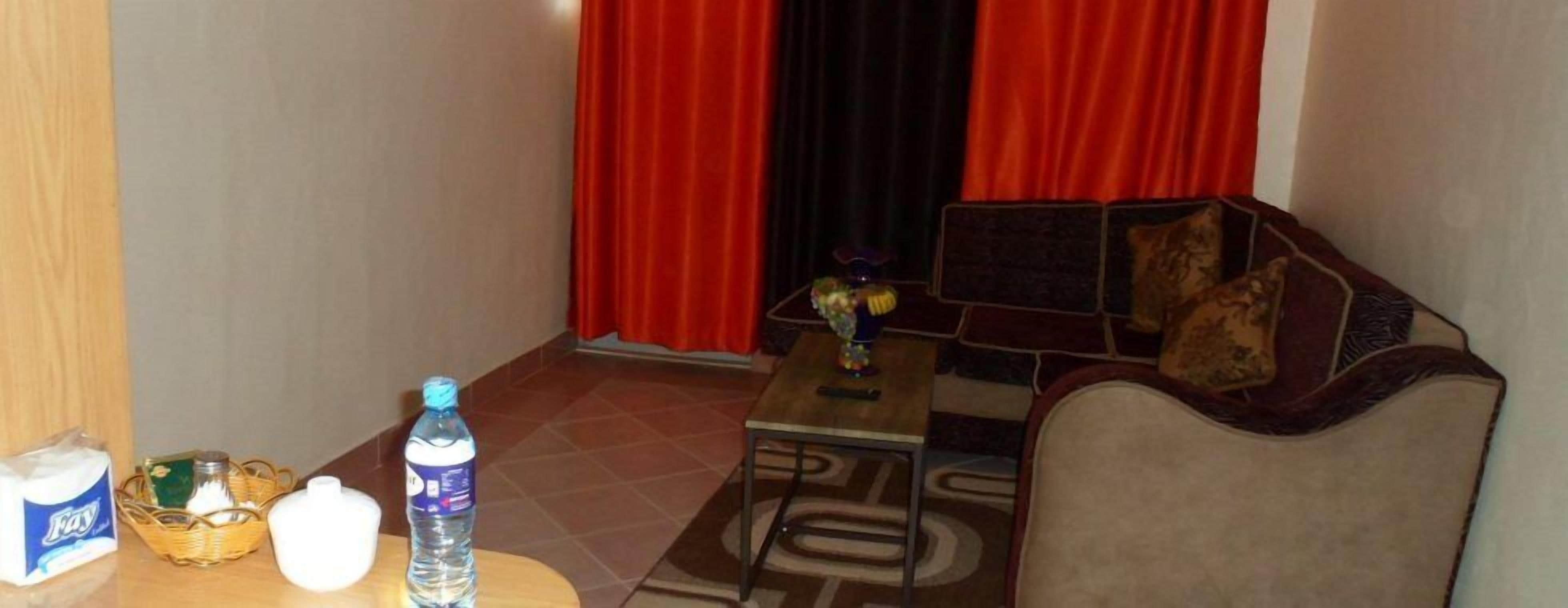 Habitación de hotel con sofá, una mesita, una botella de agua, una cesta y una caja de pañuelos.