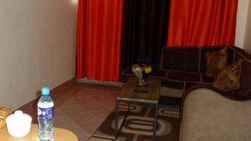 A hotel room with a sofa, a small table, a bottle of water, a basket, and a box of tissues.