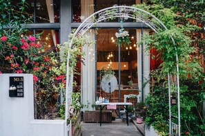 A garden entrance with a white archway, potted plants, and a table with items on it.