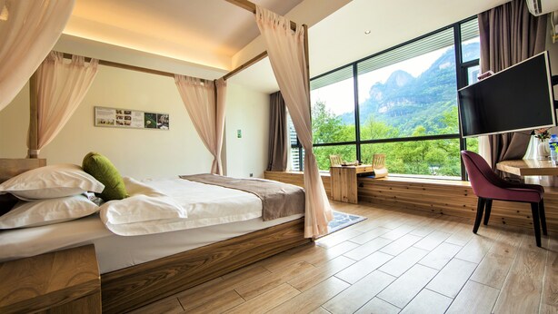Une chambre à coucher avec un lit en bois, un bureau, une chaise et une grande fenêtre donnant sur une vue imprenable sur les montagnes.
