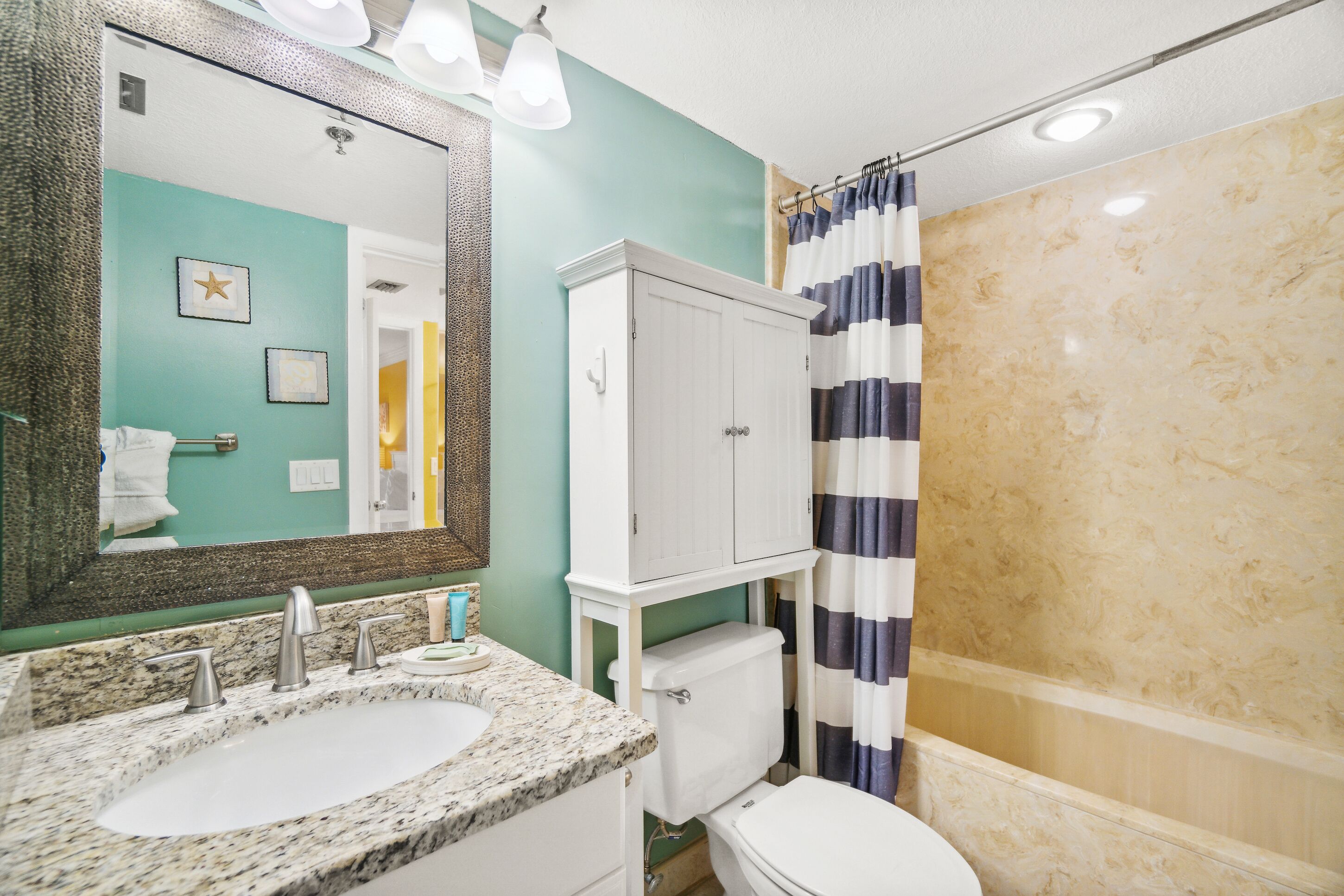 Bagno con lavabo su piano in granito, vaso bianco, mobile e doccia con tende a righe.