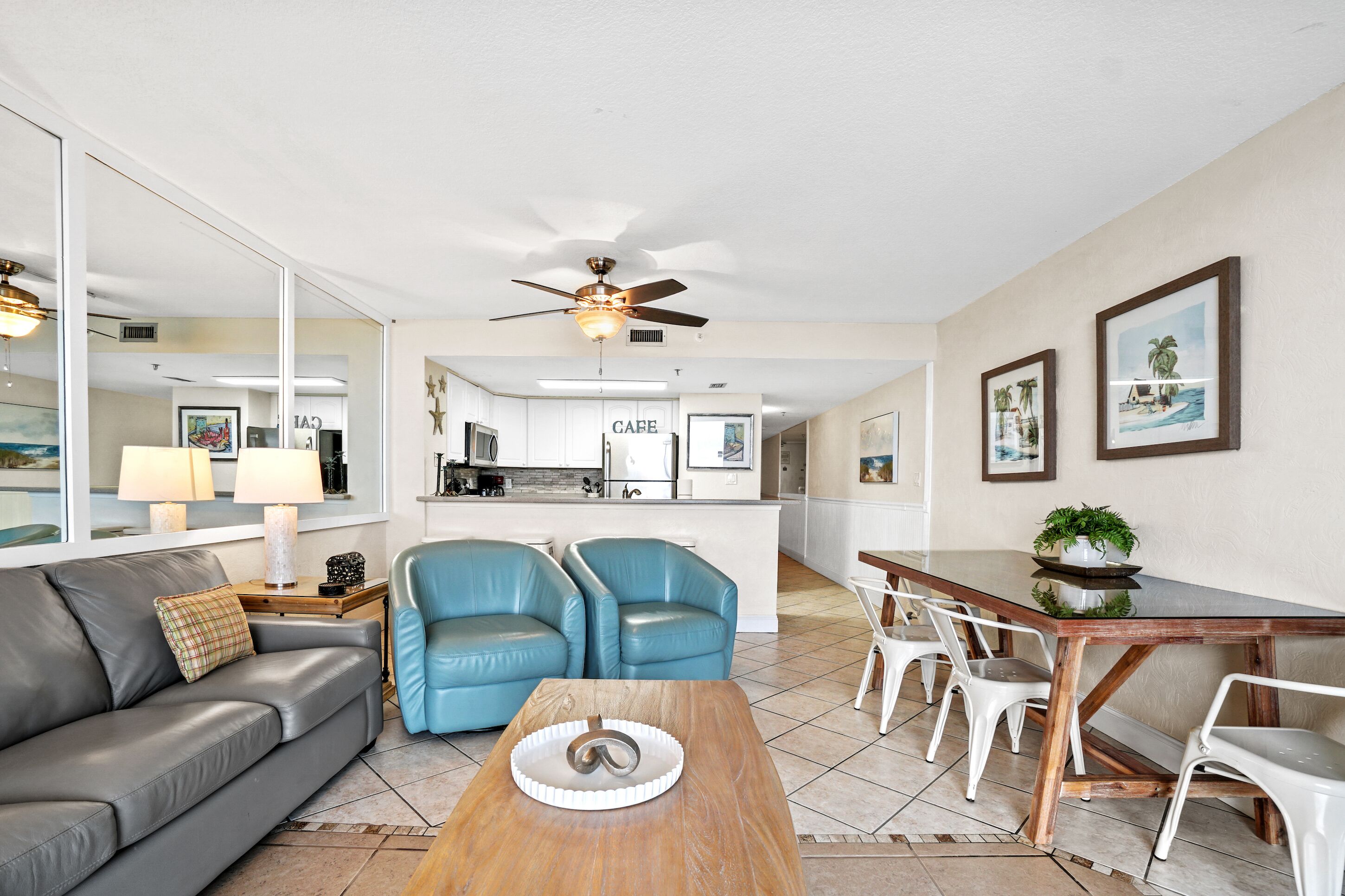 A modern living room with a grey sofa, blue armchairs, a wooden coffee table, and a dining area with white chairs.