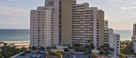 A high-rise hotel with multiple floors, a parking lot, and a view of the ocean.