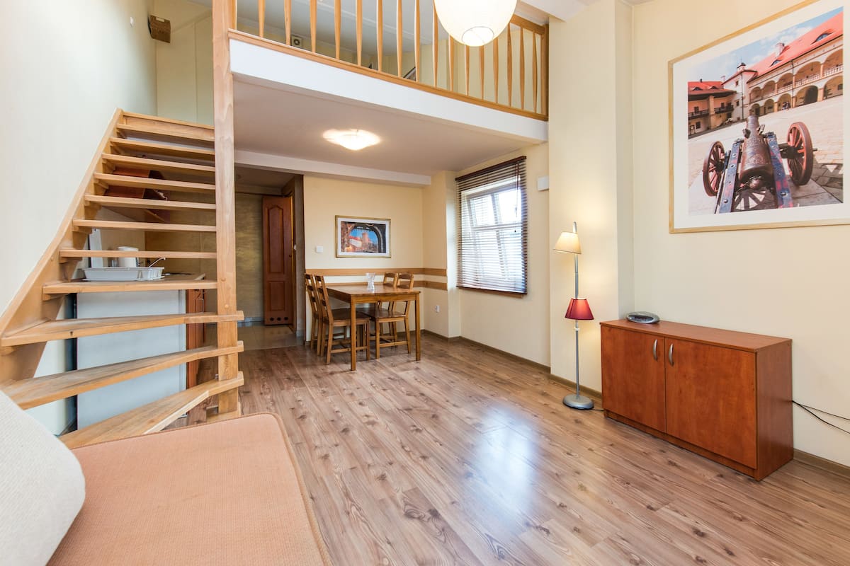 Una habitación amplia con una escalera de madera, un comedor y un cuadro grande en la pared.