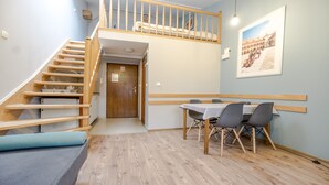A room with a wooden staircase, a dining table with chairs, and a framed picture on the wall. - Apartamenty Amber (Kraków)
